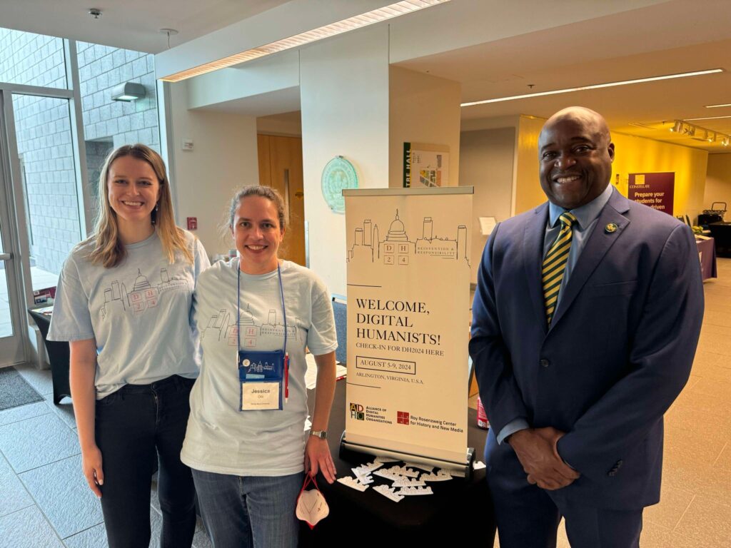 Two women and one man standing in front of a welcome sign for DH2024.
